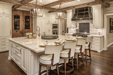 Inspiration for a huge timeless l-shaped medium tone wood floor and brown floor kitchen remodel in Omaha with a farmhouse sink, raised-panel cabinets, white cabinets, granite countertops, white backsplash, brick backsplash, stainless steel appliances, an island and beige countertops