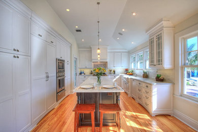 Inspiration for a mid-sized craftsman u-shaped light wood floor enclosed kitchen remodel in Tampa with a farmhouse sink, recessed-panel cabinets, white cabinets, marble countertops, white backsplash, glass tile backsplash, stainless steel appliances and an island