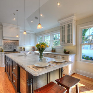 Mid-sized arts and crafts u-shaped separate kitchen in Tampa with a farmhouse sink, recessed-panel cabinets, white cabinets, marble benchtops, white splashback, glass tile splashback, stainless steel appliances, light hardwood floors and with island.