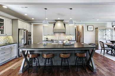 Open concept kitchen - mid-sized country l-shaped medium tone wood floor and brown floor open concept kitchen idea in Other with a farmhouse sink, recessed-panel cabinets, gray cabinets, quartz countertops, gray backsplash, cement tile backsplash, stainless steel appliances and an island