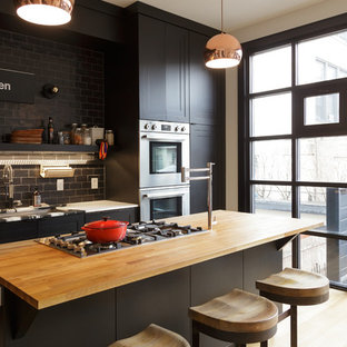Mid-sized industrial open concept kitchen pictures - Open concept kitchen - mid-sized industrial galley light wood floor open concept kitchen idea in Philadelphia with an undermount sink, shaker cabinets, black cabinets, wood countertops, gray backsplash, subway tile backsplash, stainless steel appliances and an island