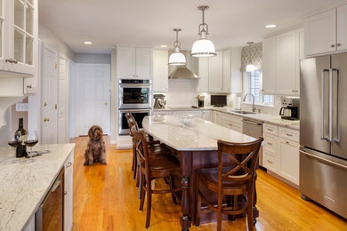 Transitional l-shaped light wood floor enclosed kitchen photo in Boston with an undermount sink, shaker cabinets, white cabinets, granite countertops, white backsplash, subway tile backsplash, stainless steel appliances and an island
