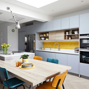 Modelo de cocina comedor contemporánea, grande, con armarios con paneles lisos, puertas de armario grises, salpicadero amarillo, salpicadero de azulejos de cerámica, una isla y encimeras blancas