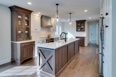 Inspiration for a large country galley medium tone wood floor open concept kitchen remodel in Philadelphia with a farmhouse sink, shaker cabinets, white cabinets, quartz countertops, white backsplash, ceramic backsplash, stainless steel appliances, an island and white countertops