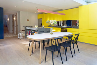 Design ideas for a large contemporary galley kitchen/diner in London with flat-panel cabinets, yellow cabinets, mirror splashback, integrated appliances, an island, beige floors and grey worktops.
