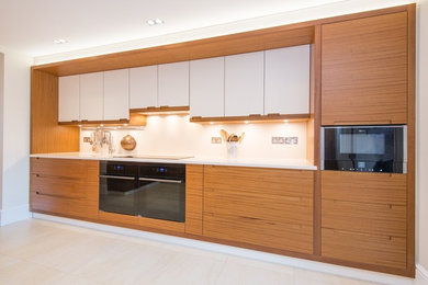 Design ideas for a medium sized contemporary galley open plan kitchen in London with a double-bowl sink, flat-panel cabinets, dark wood cabinets, engineered stone countertops, white splashback, stone slab splashback, black appliances, ceramic flooring and no island.