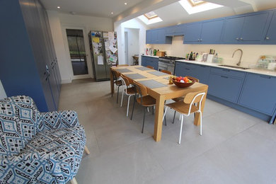 Medium sized contemporary single-wall kitchen/diner in London with a double-bowl sink, shaker cabinets, blue cabinets, composite countertops, white splashback, stone slab splashback, stainless steel appliances, ceramic flooring, no island, grey floors and white worktops.