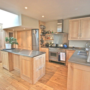 Photo of a large traditional l-shaped kitchen in London with an integrated sink, shaker cabinets, light wood cabinets, stainless steel benchtops, metallic splashback, stainless steel appliances, light hardwood floors and with island.