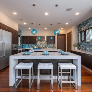 Immagine di una cucina a L tropicale con 2 o più isole, ante lisce, ante in legno bruno, paraspruzzi blu, paraspruzzi con piastrelle a listelli, elettrodomestici in acciaio inossidabile, pavimento in legno massello medio e top bianco