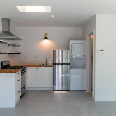 Inspiration for a small contemporary l-shaped concrete floor open concept kitchen remodel in Los Angeles with a single-bowl sink, flat-panel cabinets, white cabinets, wood countertops, white backsplash, ceramic backsplash, stainless steel appliances, no island and brown countertops