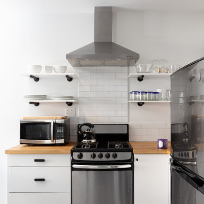 Open concept kitchen - small contemporary l-shaped concrete floor open concept kitchen idea in Los Angeles with a single-bowl sink, flat-panel cabinets, white cabinets, wood countertops, white backsplash, ceramic backsplash, stainless steel appliances, no island and brown countertops