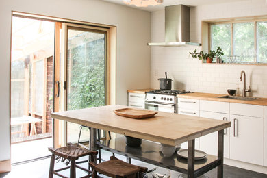 Foto de cocina comedor lineal escandinava pequeña con encimera de madera, electrodomésticos de acero inoxidable, una isla, fregadero encastrado, puertas de armario blancas y salpicadero blanco