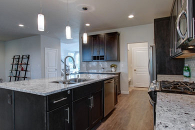 Example of a classic u-shaped medium tone wood floor open concept kitchen design in Other with a double-bowl sink, flat-panel cabinets, dark wood cabinets, solid surface countertops, multicolored backsplash, ceramic backsplash, stainless steel appliances and an island