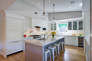 Example of a mid-sized transitional l-shaped medium tone wood floor open concept kitchen design in San Francisco with a farmhouse sink, shaker cabinets, gray cabinets, quartz countertops, white backsplash, ceramic backsplash, stainless steel appliances and an island