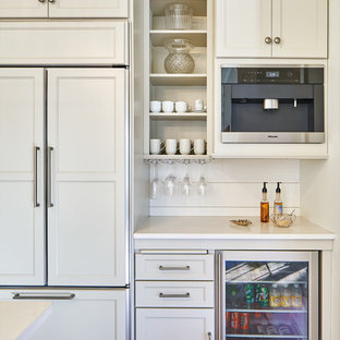 Idée de décoration pour une cuisine américaine tradition de taille moyenne avec un évier de ferme, un placard à porte shaker, des portes de placard grises, un plan de travail en granite, une crédence blanche, une crédence en bois, un électroménager en acier inoxydable, un sol en bois clair, un îlot central et un plan de travail blanc.