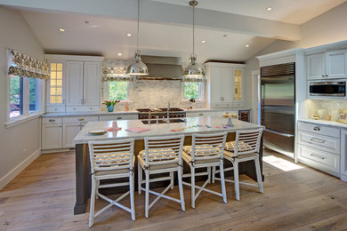Example of a large transitional l-shaped medium tone wood floor open concept kitchen design in San Francisco with an undermount sink, recessed-panel cabinets, white cabinets, marble countertops, white backsplash, stone tile backsplash, stainless steel appliances and an island