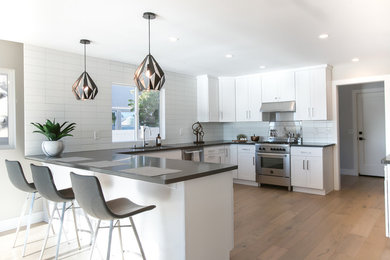 Mid-sized minimalist u-shaped light wood floor and beige floor kitchen photo in San Francisco with a drop-in sink, shaker cabinets, white cabinets, quartzite countertops, white backsplash, ceramic backsplash, stainless steel appliances and a peninsula