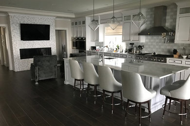Inredning av ett klassiskt mellanstort linjärt kök med öppen planlösning, med en undermonterad diskho, luckor med infälld panel, vita skåp, marmorbänkskiva, vitt stänkskydd, stänkskydd i porslinskakel, rostfria vitvaror, mörkt trägolv, en köksö och brunt golv