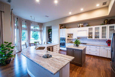 Eat-in kitchen - large contemporary l-shaped medium tone wood floor and brown floor eat-in kitchen idea in Other with an undermount sink, glass-front cabinets, white cabinets, granite countertops, white backsplash, porcelain backsplash, stainless steel appliances, two islands and multicolored countertops