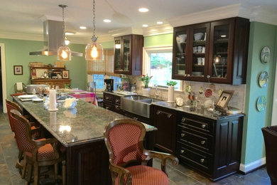 Large elegant galley slate floor eat-in kitchen photo in Other with a farmhouse sink, raised-panel cabinets, dark wood cabinets, granite countertops, beige backsplash, stone tile backsplash, stainless steel appliances and an island