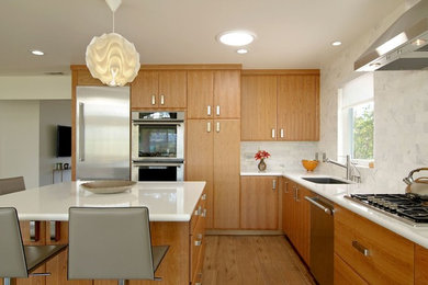 Example of a mid-sized transitional l-shaped medium tone wood floor and brown floor open concept kitchen design in Los Angeles with an undermount sink, flat-panel cabinets, light wood cabinets, white backsplash, marble backsplash, stainless steel appliances and an island