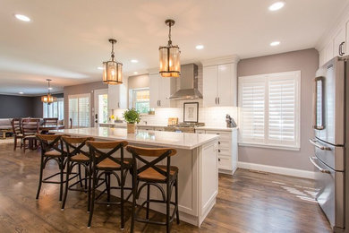 Inspiration for a large transitional l-shaped medium tone wood floor and brown floor eat-in kitchen remodel in Denver with a farmhouse sink, shaker cabinets, white cabinets, quartzite countertops, white backsplash, subway tile backsplash, stainless steel appliances and an island