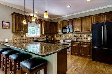 Example of a large transitional u-shaped medium tone wood floor and brown floor eat-in kitchen design in New York with a drop-in sink, raised-panel cabinets, medium tone wood cabinets, granite countertops, brown backsplash, stone tile backsplash, black appliances, a peninsula and brown countertops