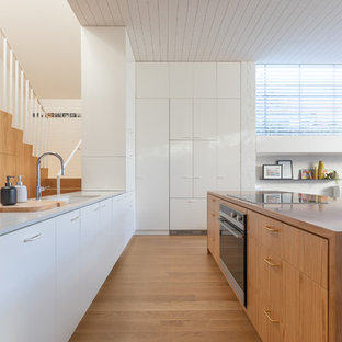 Inspiration for a small contemporary galley kitchen in Melbourne with an undermount sink, recessed-panel cabinets, white cabinets, black appliances, light hardwood floors, multiple islands, brown floor and multi-coloured benchtop.