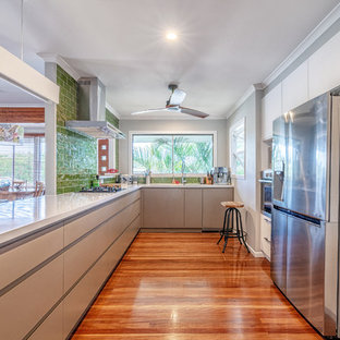 Large contemporary u-shaped kitchen in Brisbane with flat-panel cabinets, beige cabinets, green splashback, ceramic splashback, stainless steel appliances, medium hardwood floors, a peninsula, brown floor and white benchtop.