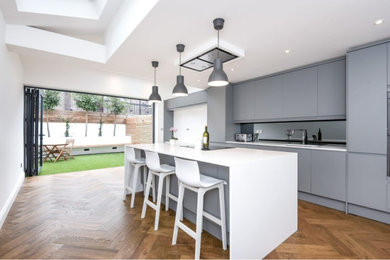 Photo of a modern kitchen in London with flat-panel cabinets, grey cabinets, metallic splashback, medium hardwood flooring, an island, brown floors and white worktops.