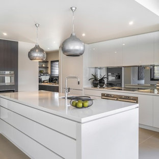 Contemporary kitchen in Melbourne with an undermount sink, flat-panel cabinets, white cabinets, mirror splashback, stainless steel appliances, with island, grey floor and white benchtop.