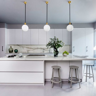 Large contemporary l-shaped kitchen in London with flat-panel cabinets, composite countertops, white splashback, stone slab splashback, an island, white worktops, white cabinets, white appliances and grey floors.