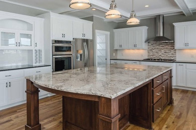 Example of a large trendy l-shaped medium tone wood floor and brown floor kitchen design in Minneapolis with shaker cabinets, white cabinets, granite countertops, white backsplash, subway tile backsplash, stainless steel appliances and an island