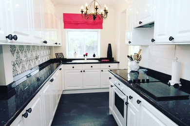 Design ideas for a small contemporary galley enclosed kitchen in Kent with a built-in sink, raised-panel cabinets, white cabinets, laminate countertops, white splashback, ceramic splashback, white appliances, laminate floors, no island, grey floors and black worktops.