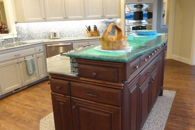 Example of a large beach style l-shaped dark wood floor eat-in kitchen design in Seattle with an undermount sink, recessed-panel cabinets, dark wood cabinets, green backsplash, glass tile backsplash, stainless steel appliances, an island, glass countertops and turquoise countertops