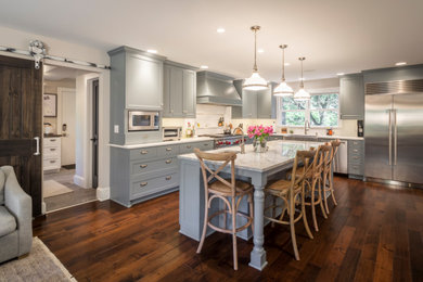 Kitchen - large transitional l-shaped medium tone wood floor and brown floor kitchen idea in Minneapolis with a farmhouse sink, shaker cabinets, gray cabinets, white backsplash, stainless steel appliances, an island and gray countertops