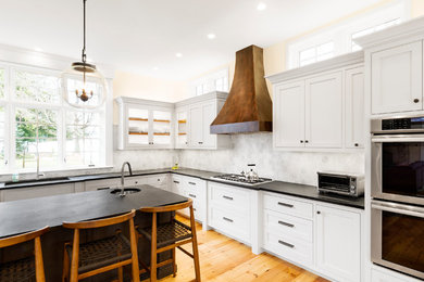 Example of a large transitional l-shaped light wood floor eat-in kitchen design in Boston with an undermount sink, shaker cabinets, white cabinets, soapstone countertops, white backsplash, stone tile backsplash, paneled appliances and an island