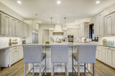 Inspiration for a large transitional u-shaped porcelain tile and brown floor eat-in kitchen remodel in Austin with an undermount sink, recessed-panel cabinets, distressed cabinets, granite countertops, white backsplash, ceramic backsplash, stainless steel appliances and two islands