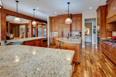 Kitchen - large transitional dark wood floor kitchen idea in Austin with a farmhouse sink, raised-panel cabinets, medium tone wood cabinets, granite countertops, paneled appliances and two islands