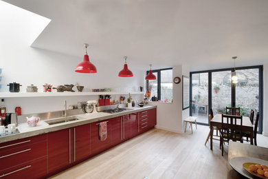 ロンドンにある中くらいなコンテンポラリースタイルのおしゃれなキッチン (ダブルシンク、赤いキャビネット、コンクリートカウンター、メタリックのキッチンパネル、シルバーの調理設備、アイランドなし) の写真