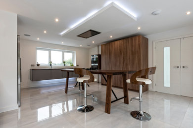 Large contemporary single-wall kitchen/diner in Cheshire with a double-bowl sink, flat-panel cabinets, medium wood cabinets, wood worktops, grey splashback, glass sheet splashback, black appliances, porcelain flooring, an island and white floors.