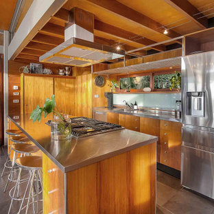 Design ideas for a tropical kitchen in Sydney with an integrated sink, flat-panel cabinets, medium wood cabinets, stainless steel benchtops, stainless steel appliances, with island and grey floor.