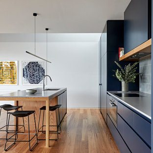Photo of a large modern galley eat-in kitchen in Melbourne with a double-bowl sink, flat-panel cabinets, blue cabinets, quartz benchtops, grey splashback, ceramic splashback, black appliances, with island, grey benchtop, medium hardwood floors and brown floor.