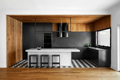 Inredning av ett modernt svart svart kök, med en enkel diskho, släta luckor, svarta skåp, bänkskiva i betong, svart stänkskydd, stänkskydd i porslinskakel, svarta vitvaror, klinkergolv i keramik, en köksö och svart golv
