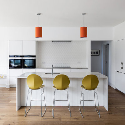 Example of a trendy l-shaped dark wood floor and brown floor eat-in kitchen design in Other with an undermount sink, flat-panel cabinets, white cabinets, white backsplash, stainless steel appliances and an island