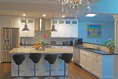 Klassisk inredning av ett l-kök, med en undermonterad diskho, skåp i shakerstil, vita skåp, granitbänkskiva, vitt stänkskydd, stänkskydd i stenkakel, rostfria vitvaror, mörkt trägolv och en köksö