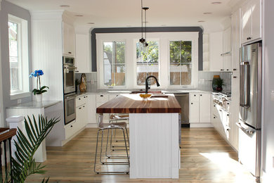 Example of a large arts and crafts u-shaped light wood floor kitchen design in Denver with a farmhouse sink, shaker cabinets, white cabinets, white backsplash, glass tile backsplash, stainless steel appliances and an island