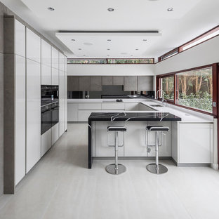 Inspiration for a large contemporary u-shaped kitchen in London with a submerged sink, flat-panel cabinets, white cabinets, black splashback, black appliances, a breakfast bar, grey floors and white worktops.