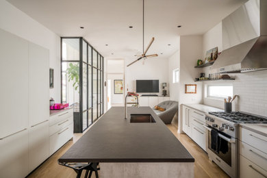 Mid-sized 1950s galley light wood floor and brown floor eat-in kitchen photo in Houston with an undermount sink, flat-panel cabinets, gray cabinets, quartz countertops, white backsplash, subway tile backsplash, stainless steel appliances, an island and black countertops