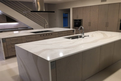 Inspiration for a large modern limestone floor and beige floor kitchen remodel in Houston with an undermount sink, flat-panel cabinets, medium tone wood cabinets, quartz countertops, beige backsplash, paneled appliances, two islands and beige countertops
